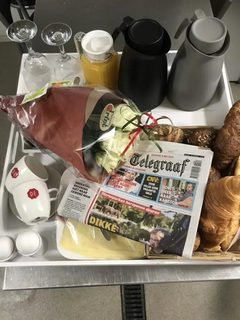 Gevuld ontbijtdienblad met bloemen, krant, koffie en verse broodjes