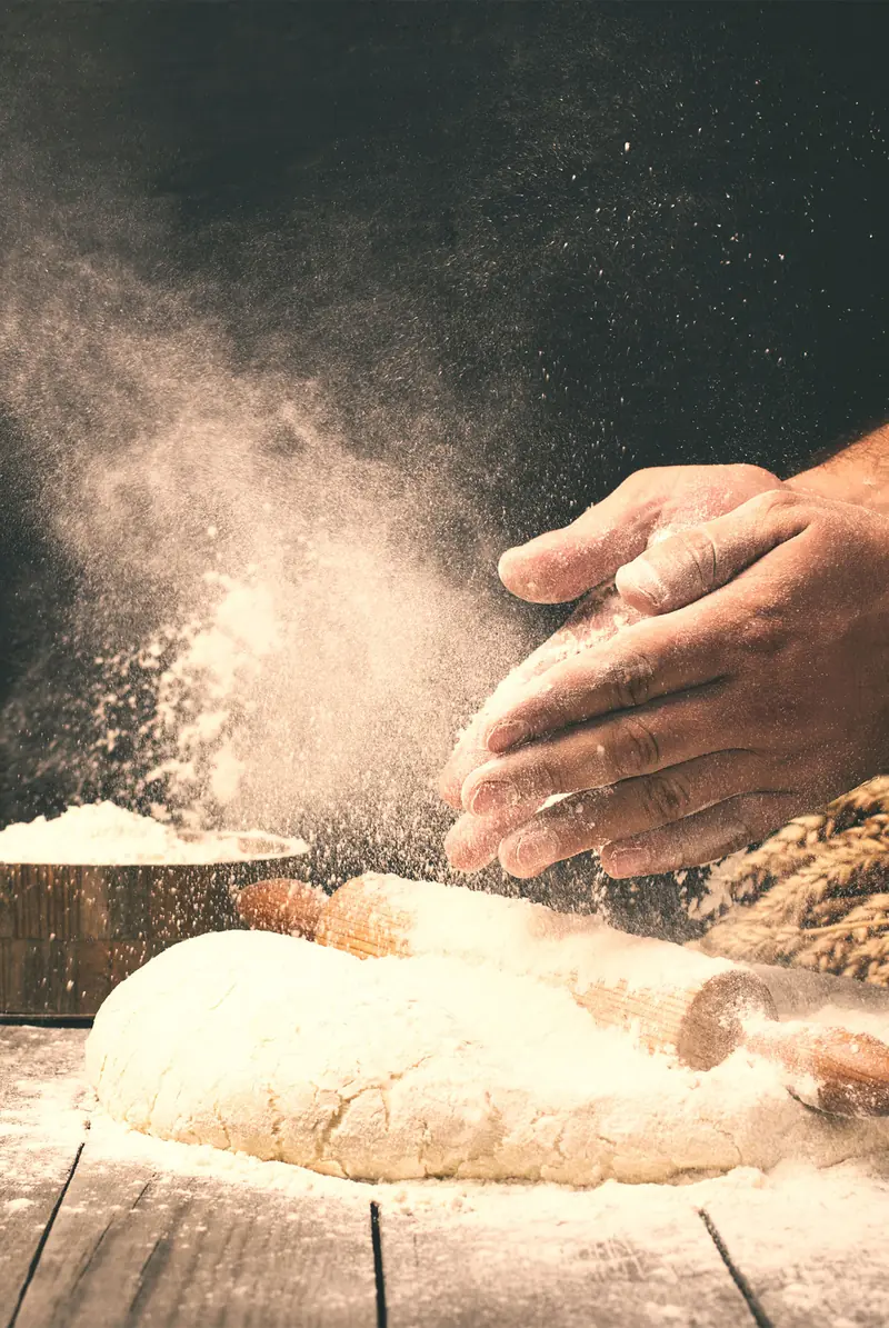 Bakkershanden met deeg op een met bloem bestoven werkbank